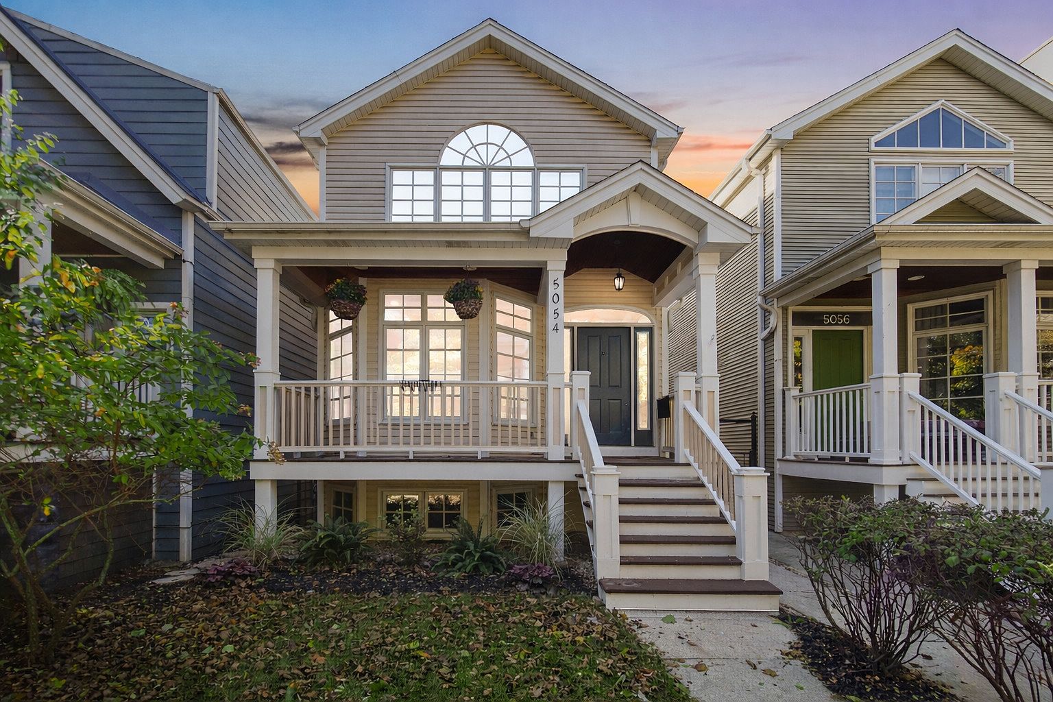 Front elevation of 5054 N Claremont Avenue at twilight, showing the covered porch with bay window, double-height arched window above the entry, and the warm porch light spilling onto the painted wood siding